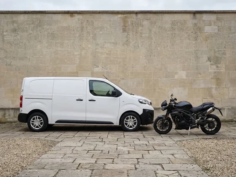 Uma carrinha comercial branca ao lado de uma mota junto a um muro de pedra